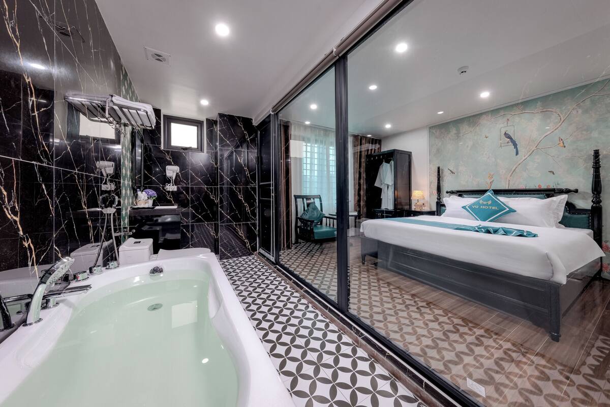 A modern hotel room with a large bed, a bathtub, and a glass-enclosed shower area.