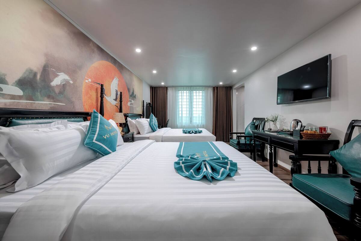 A hotel room with two beds, a desk, a TV, and a mural on the wall.