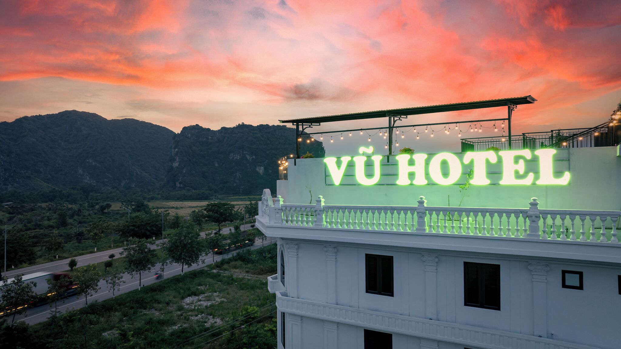 A hotel with a prominent sign reading "VÜ HOTEL" against a backdrop of a mountainous landscape and a sunset sky.