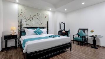 A hotel room with a bed, a desk, a chair, a small table, and a wall with a floral mural.
