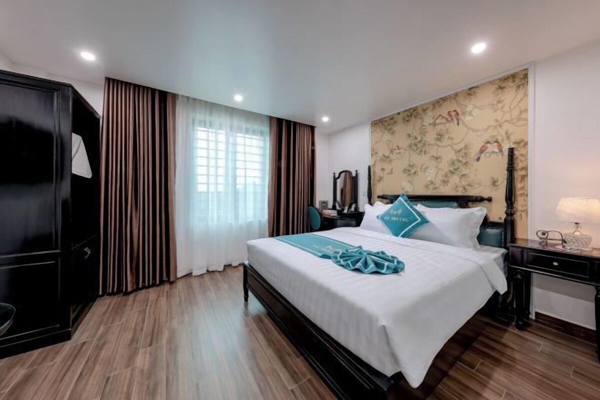 A hotel room with a large bed, a wardrobe, a desk, and a nightstand.