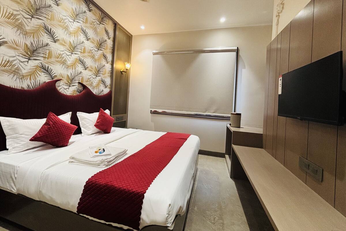 A hotel room with a bed, a TV, a mirror, and a wall with a leaf pattern.