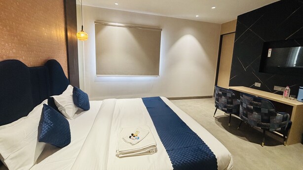 A modern hotel room with a bed, a desk, a chair, a TV, and a window. - Hotel Royal Nest (Ajmer)