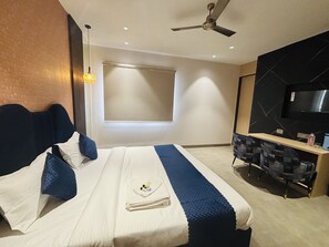A modern hotel room with a bed, a desk, a chair, a TV, and a window. - Hotel Royal Nest (Ajmer)