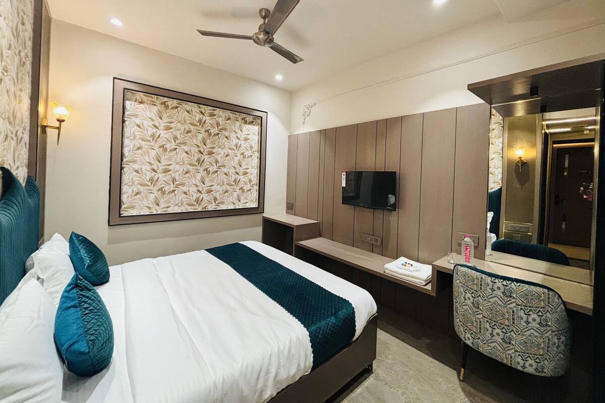 A modern hotel room with a bed, a desk, a chair, a TV, and a ceiling fan.