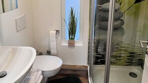 Un bagno moderno con doccia in vetro, un lavandino bianco e un piccolo oblò con una pianta.