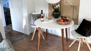 Zona pranzo con tavolo rotondo, sedie, un lampadario, un quadro e una bottiglia di vino.
