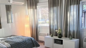 Una camera da letto moderna con un letto, un divano, un tavolino consolle bianco e un'ampia finestra con tende.