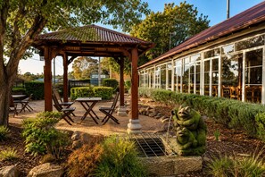 A gazebo with a table and chairs, surrounded by greenery and a stone frog statue. - Margaret River Motel (Margaret River)