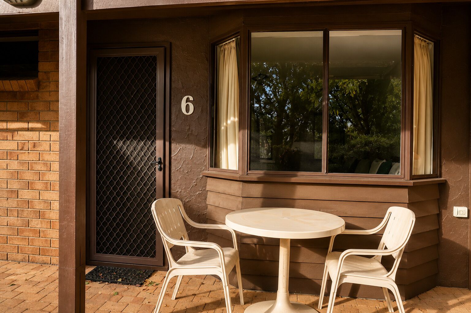 Uma área de estar no canto com uma mesa e quatro cadeiras, uma porta com um número e uma janela com cortinas.