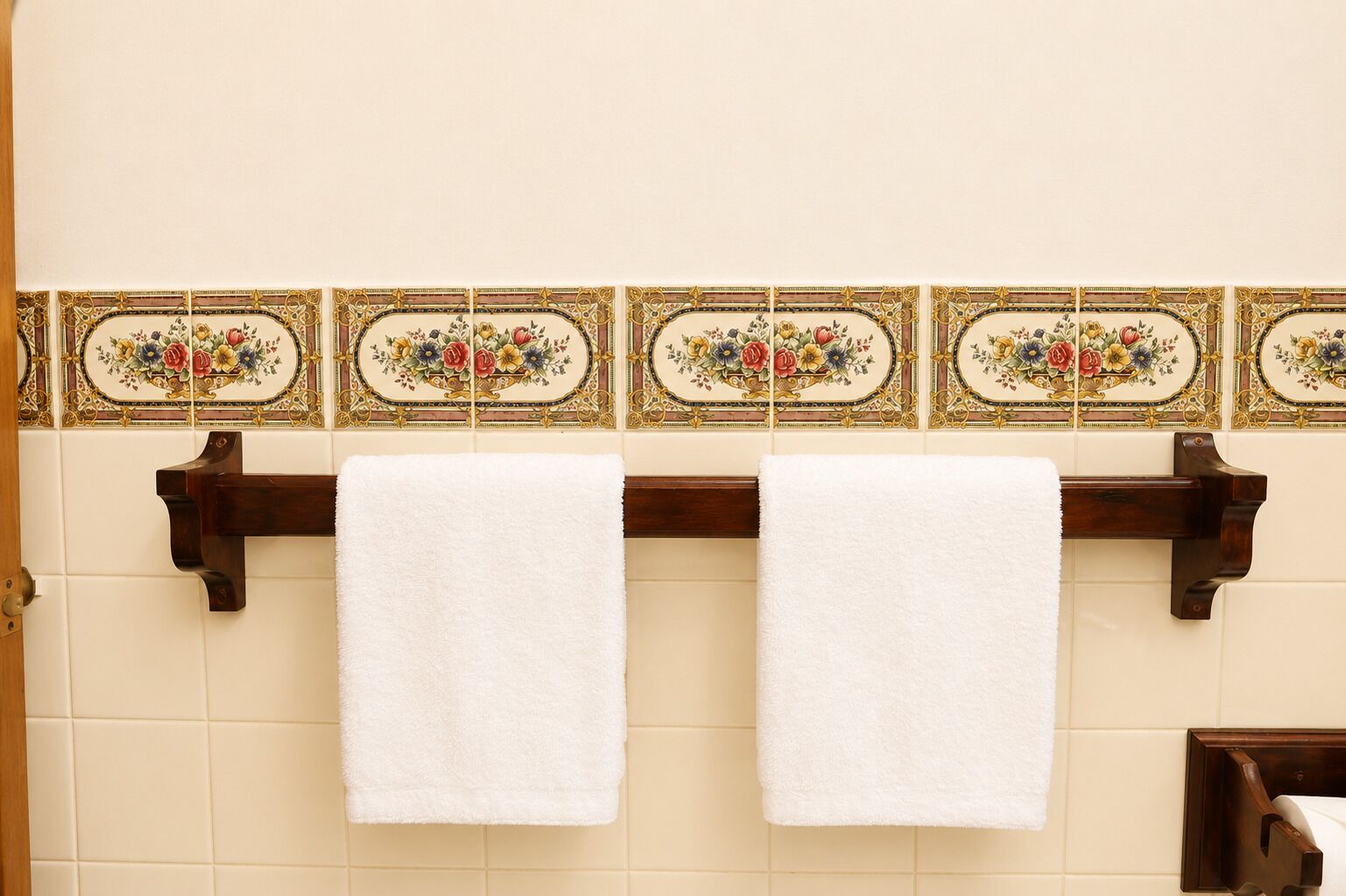 Un baño con dos toallas blancas colgadas en un toallero de madera frente a una pared con azulejos decorativos.