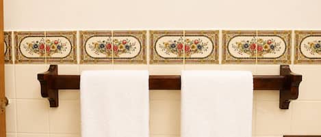 Een badkamer met twee witte handdoeken aan een houten handdoekrek, voor een muur met decoratieve tegels.
