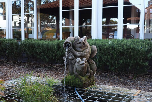 A stone fountain with water spouting from its mouth, surrounded by a metal grid and greenery. - Margaret River Motel (Margaret River)