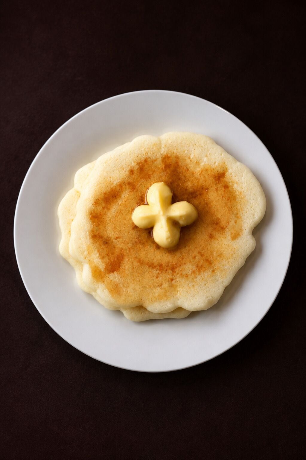 Un panqueque sobre un plato blanco con un poco de mantequilla en el centro.