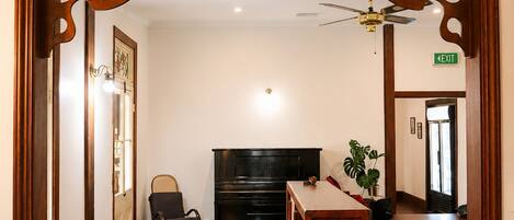 A hotel lobby with a wooden reception desk, a black piano, a wheelchair, a small stool, and a ceiling fan.