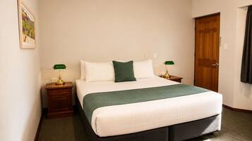 A hotel room with a large bed, two bedside tables with lamps, a door, and a painting on the wall.