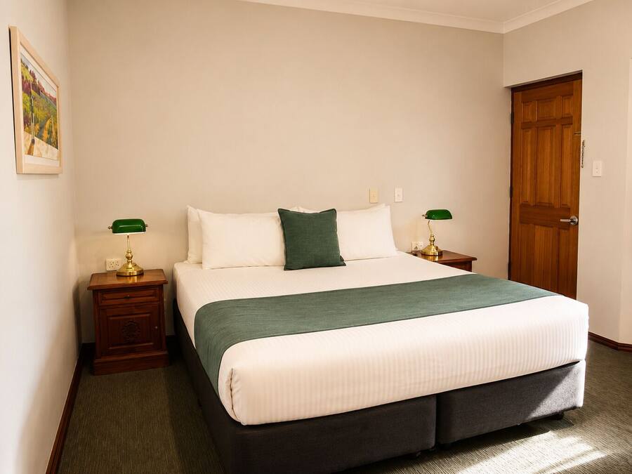 A hotel room with a large bed, two bedside tables with lamps, a door, and a painting on the wall.
