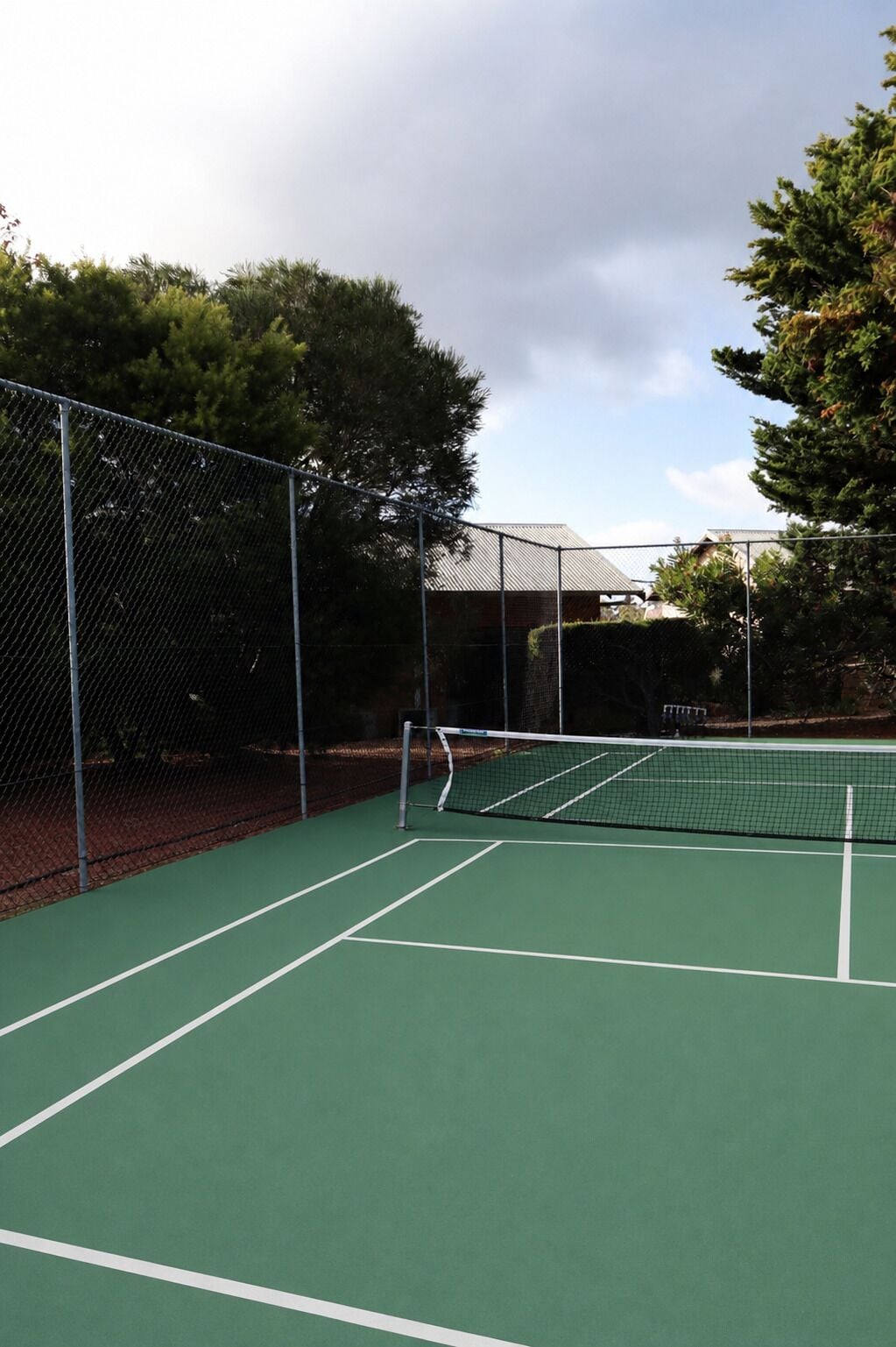 Un campo da tennis con rete, circondato da una recinzione a rete metallica e alberi.