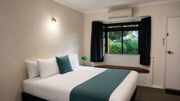 Una habitación de hotel con cama, ventana con cortinas, aire acondicionado y una puerta.