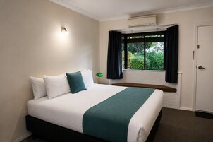 Una habitación de hotel con cama, ventana con cortinas, aire acondicionado y una puerta.