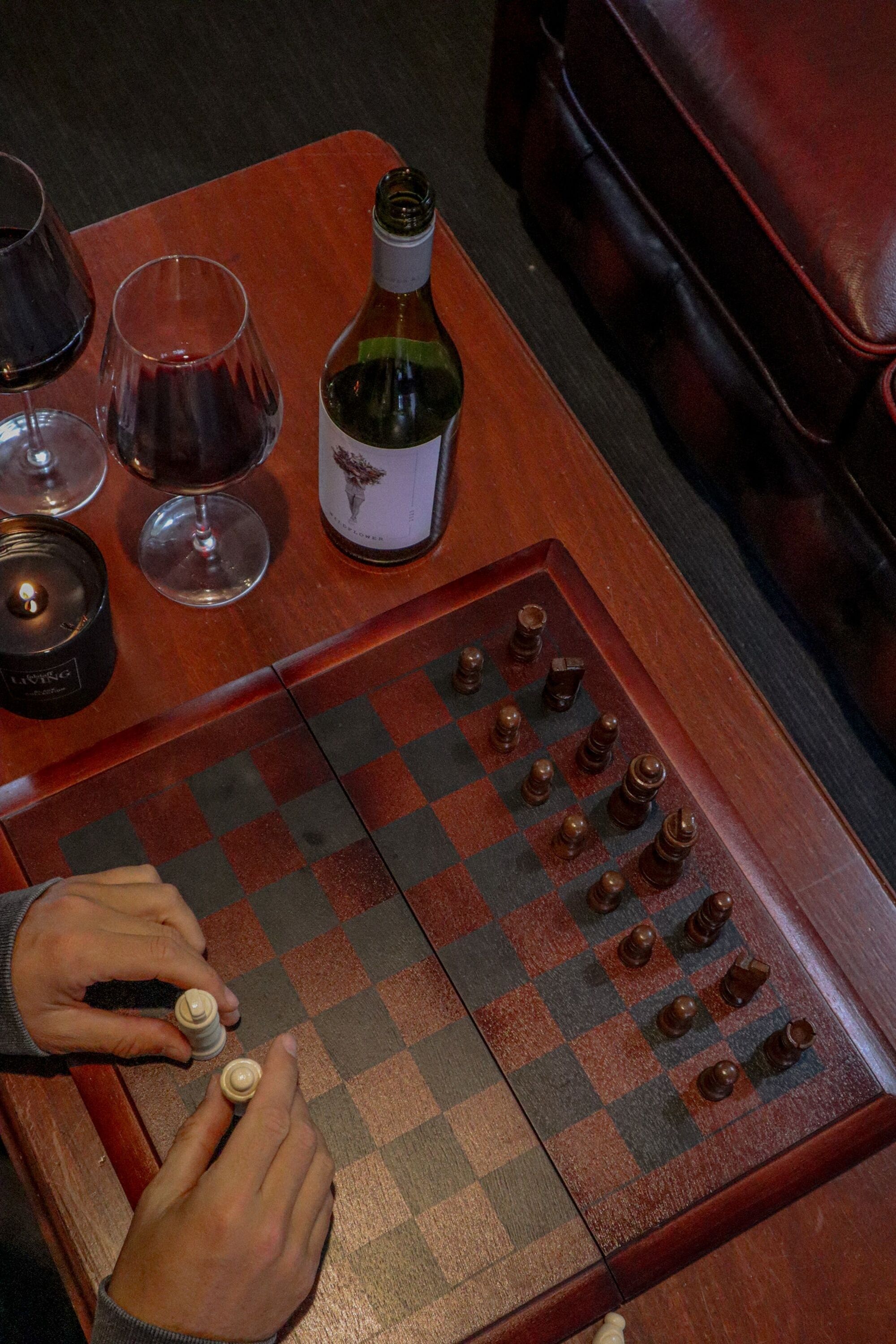 A chessboard with pieces, a bottle, and glasses on a table.