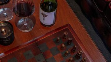 A chessboard with pieces, a bottle, and glasses on a table.