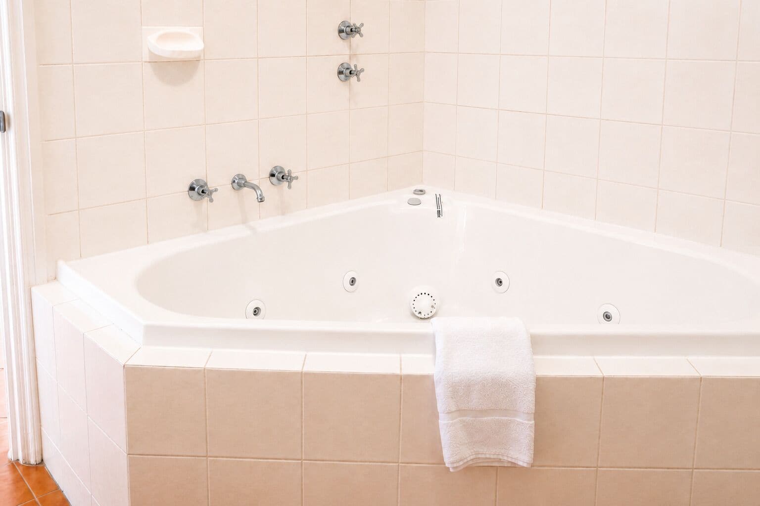 A white bathtub with multiple faucets, a built-in soap dish, and a towel on the side.