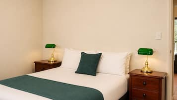 A neatly made bed with a green throw blanket, two bedside tables with lamps, and a single green pillow.