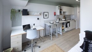 A modern kitchen with white cabinetry, a dining area with a white table and chairs, a built-in oven, and a small plant on the wall. - Modern Studios with Kitchen & Ensuite (Edinburgh)