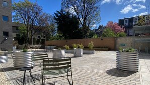 An outdoor patio area with metal benches and planters, surrounded by buildings and trees. - Modern Studios with Kitchen & Ensuite (Edinburgh)