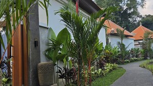A pathway leading to a building with a tiled roof, surrounded by lush greenery and a stone bench. - Tanah Wuk Villas (Abiansemal)