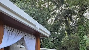 A covered outdoor seating area with a bench and a table, surrounded by lush greenery and a pool. - Tanah Wuk Villas (Abiansemal)
