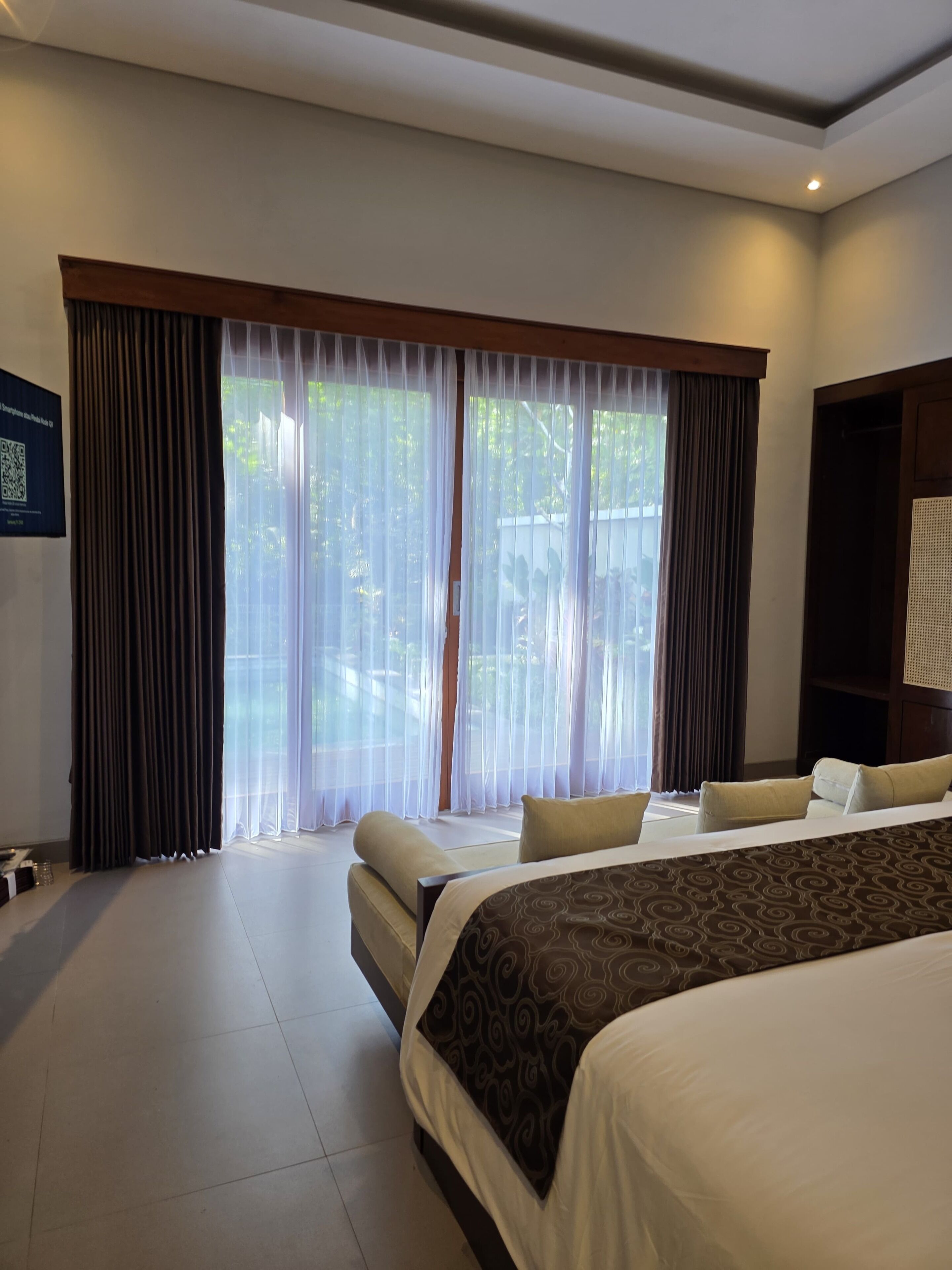 Une chambre d’hôtel avec un grand lit, un canapé et une vue sur la verdure par les fenêtres.