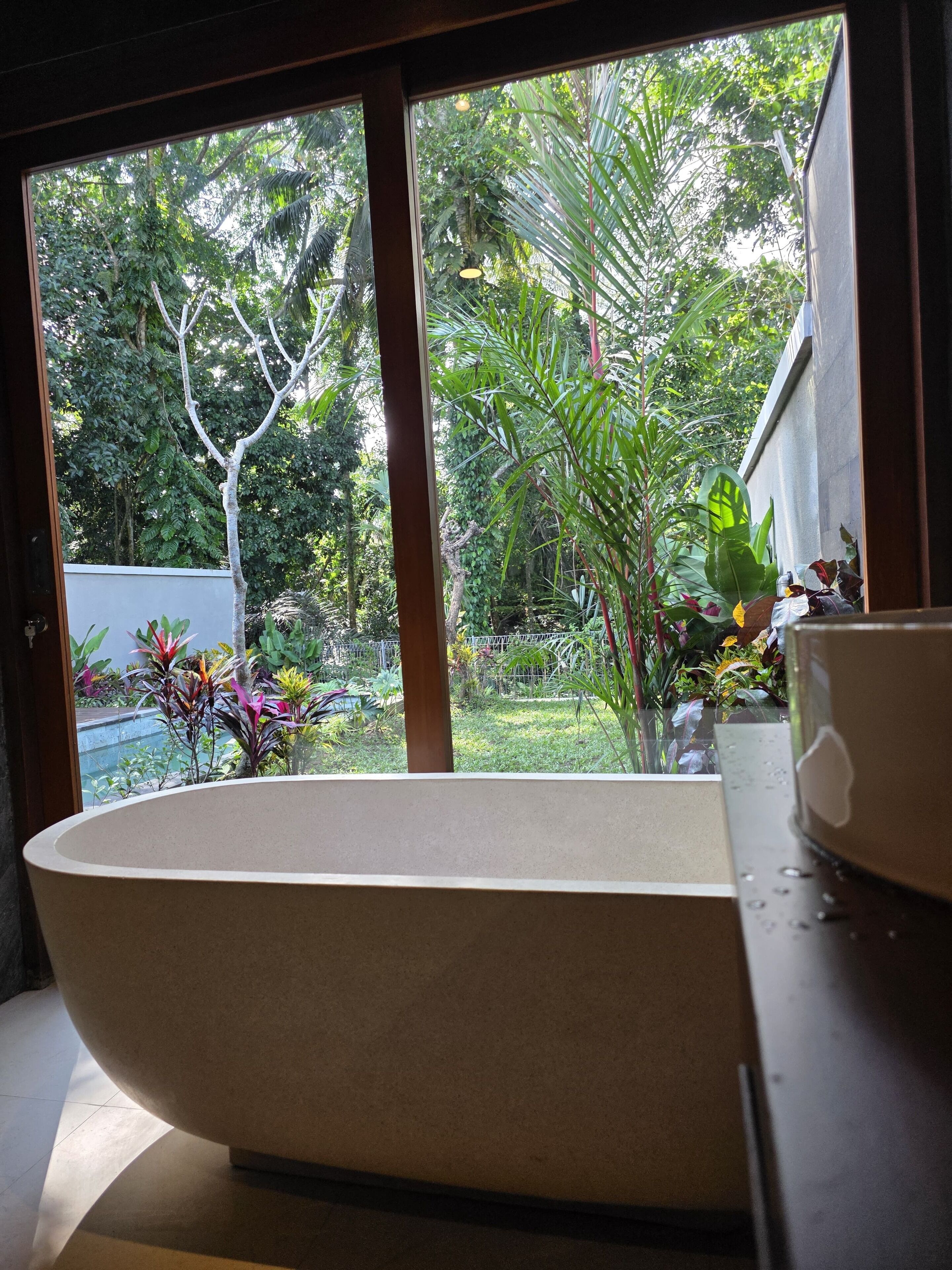 Une baignoire dans une pièce donnant sur un jardin luxuriant, visible à travers une fenêtre.