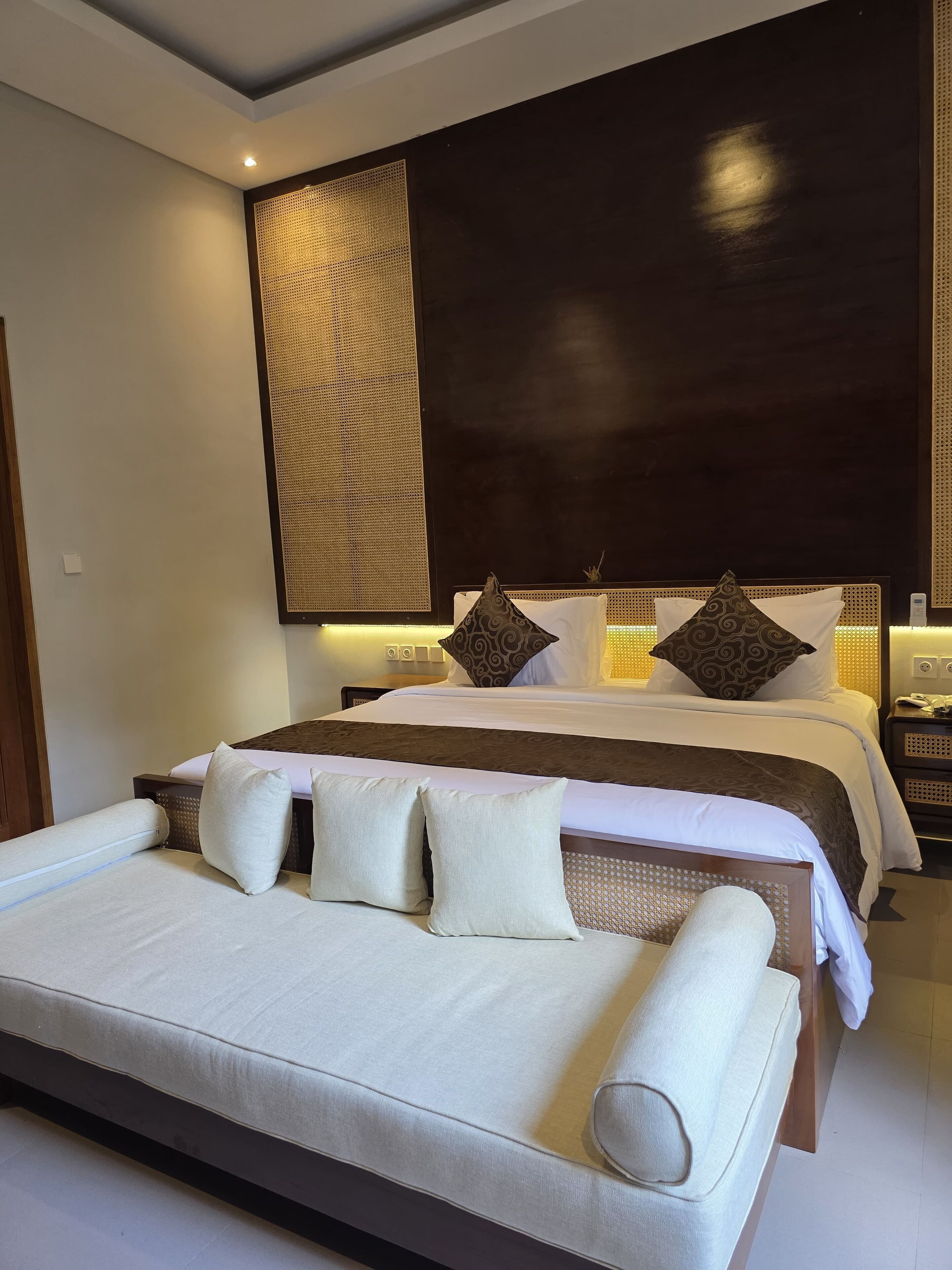 A modern hotel room with a large bed, a sofa, and a decorative wall panel.