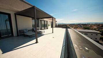 Une terrasse sur le toit dotée d’un espace salon couvert, offrant une vue sur le paysage urbain et équipée d’un ensemble de panneaux solaires.
