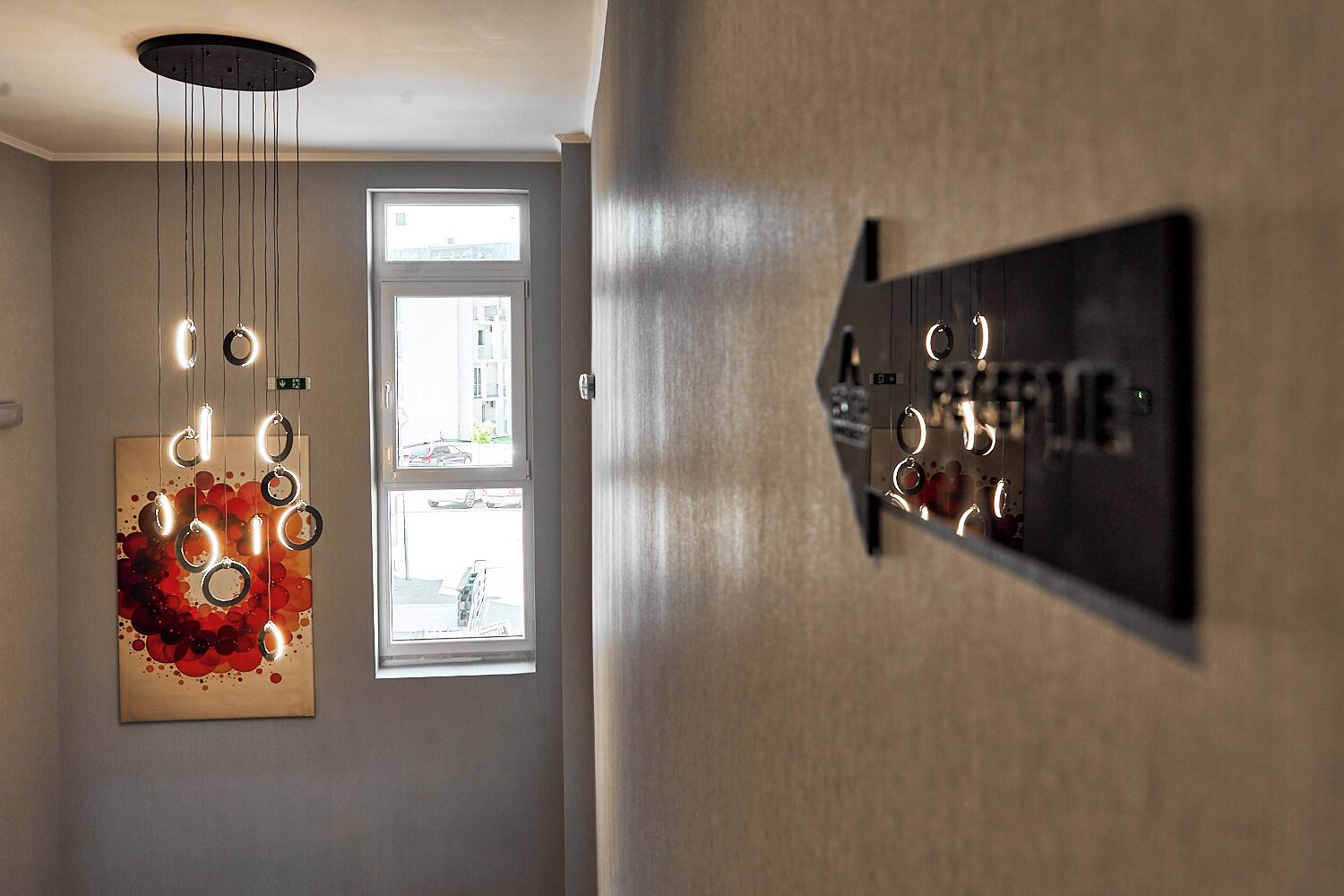 Un pasillo con un accesorio de iluminación moderno, una puerta con ventanal y un cartel en la pared.