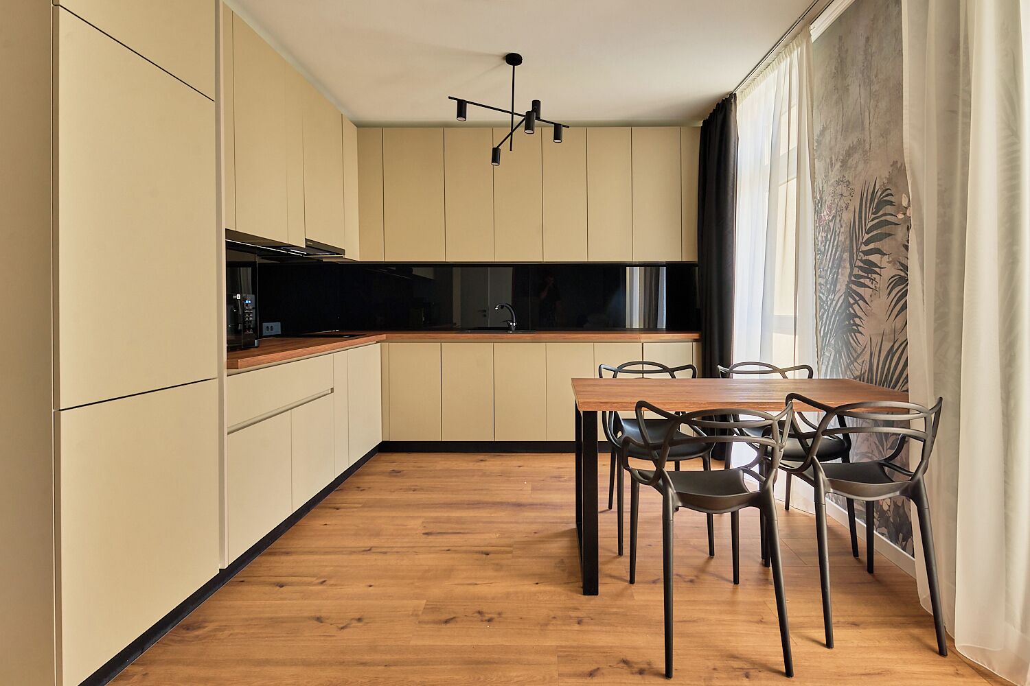 A modern kitchen with wooden flooring, a dining table with chairs, and a large window with curtains.