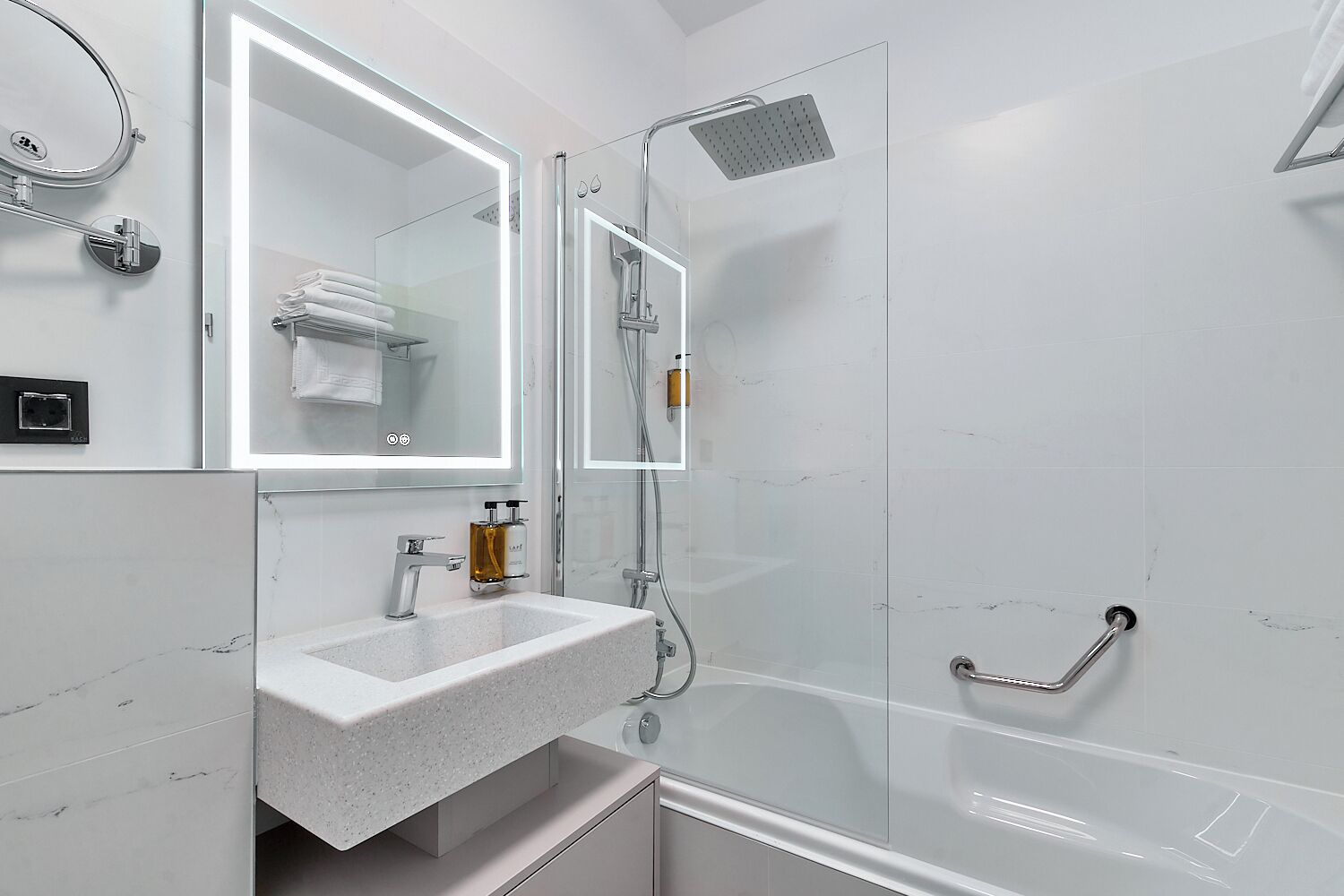 Un baño moderno con ducha de vidrio, un espejo grande y un lavamanos de mármol blanco.