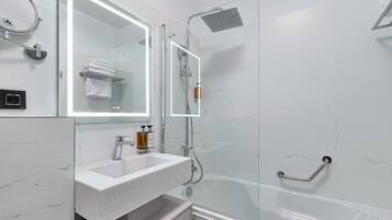 Un baño moderno con ducha de vidrio, un espejo grande y un lavamanos de mármol blanco.
