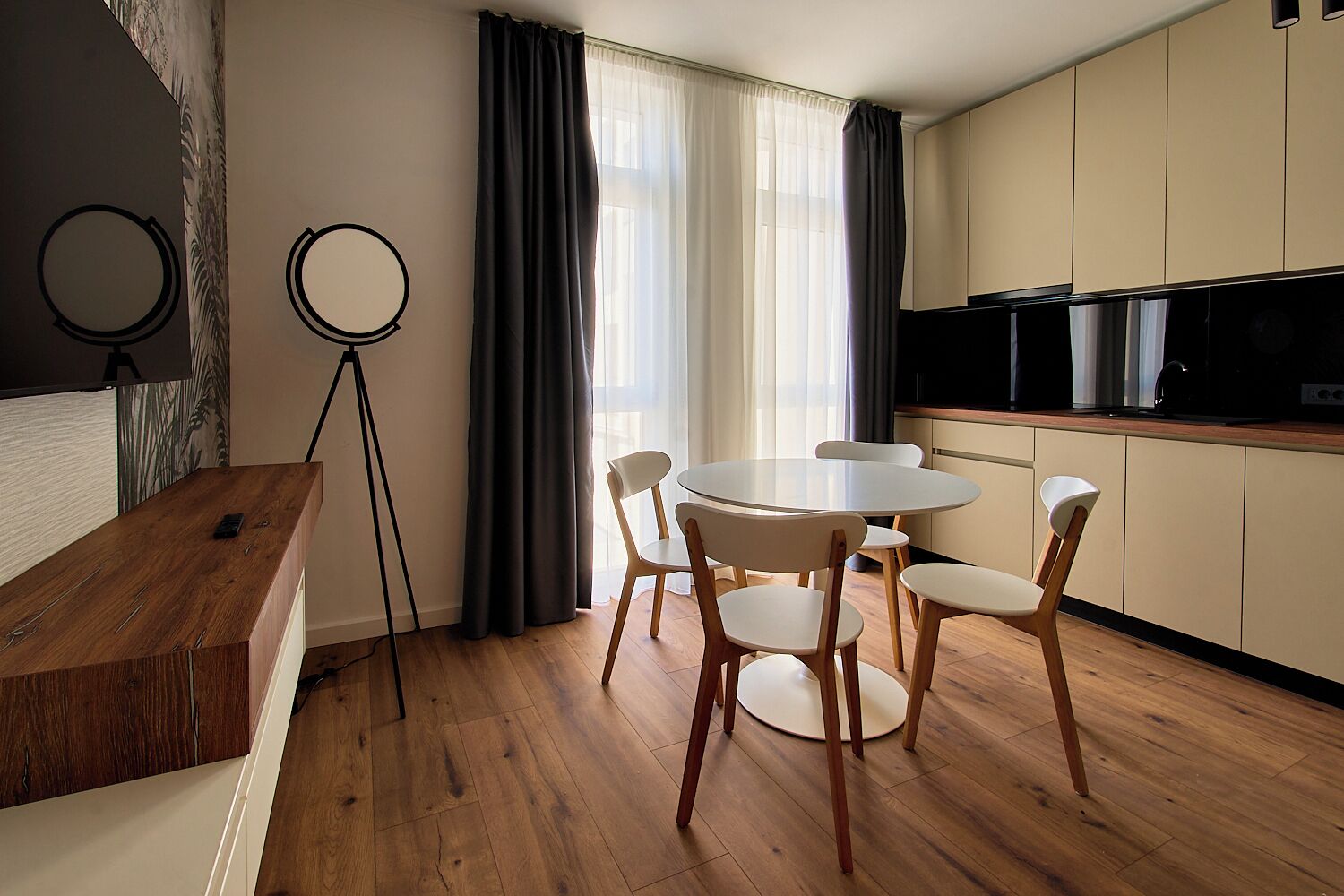 Een moderne keuken met een ronde eettafel en stoelen, een statief en een groot raam met gordijnen.