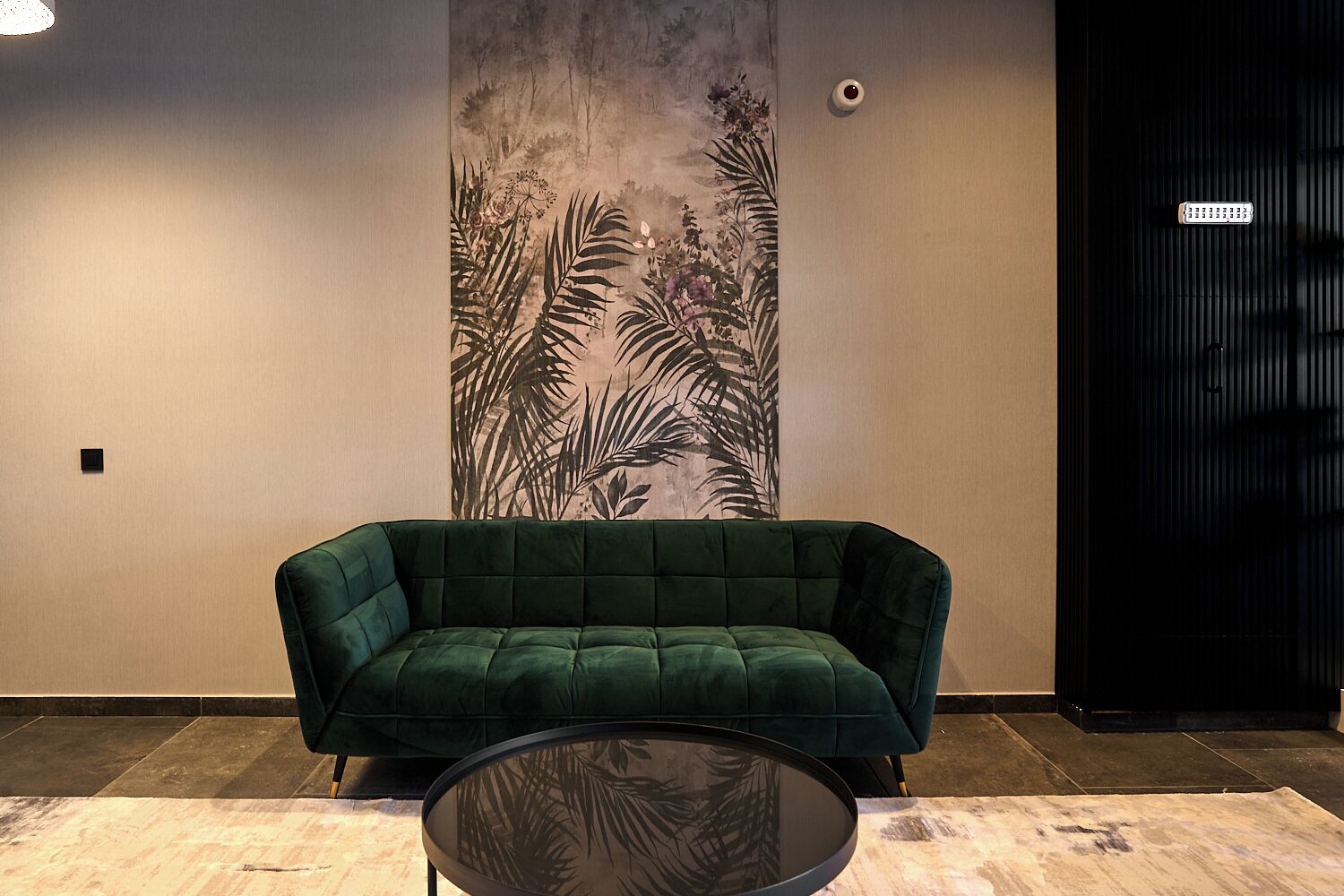 A green sofa and a round table in a room with a large wall mural of foliage.