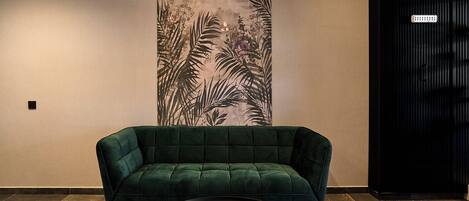 A green sofa and a round table in a room with a large wall mural of foliage.