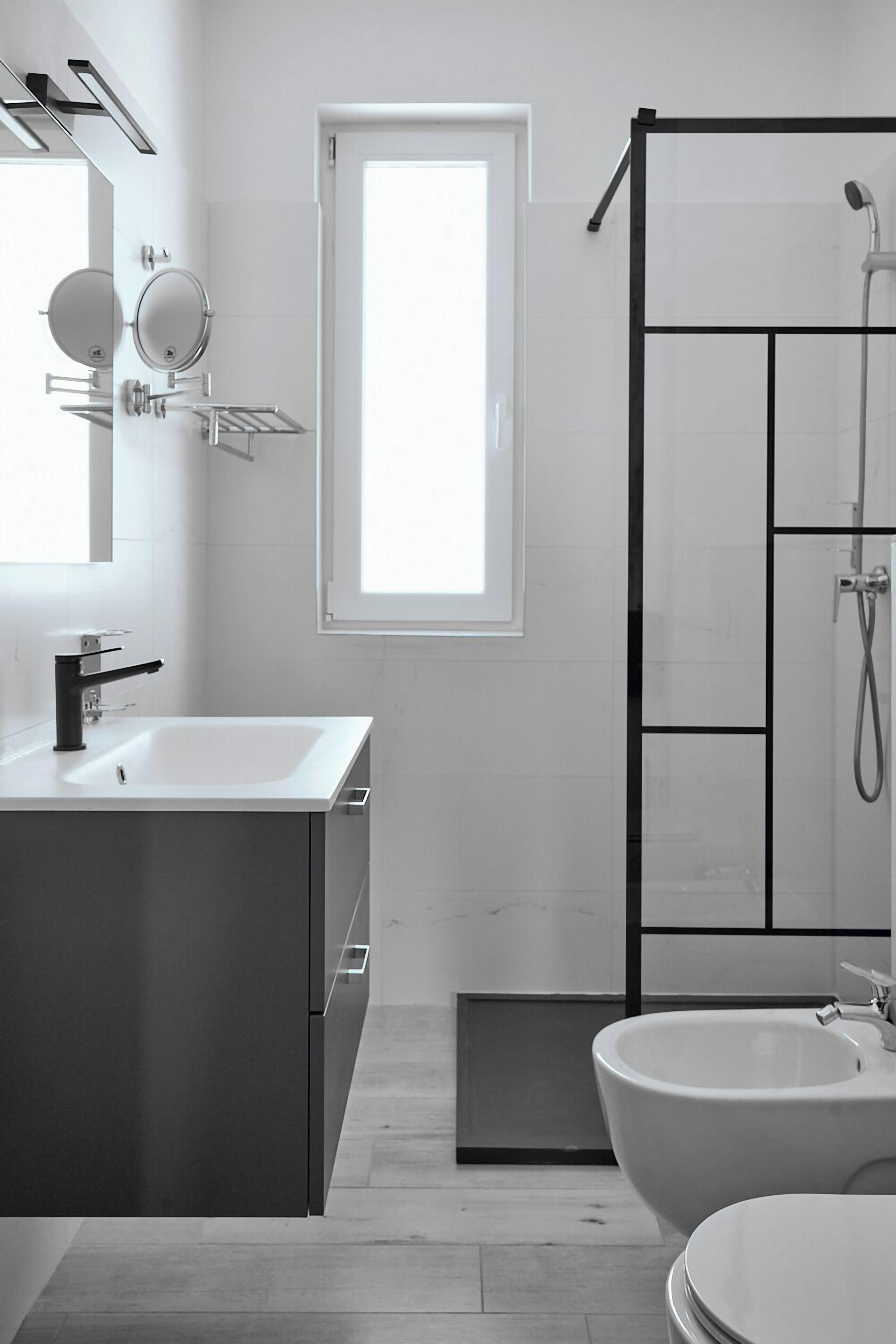 A modern bathroom with a white sink, a mirror, a shower enclosure, and a bidet.