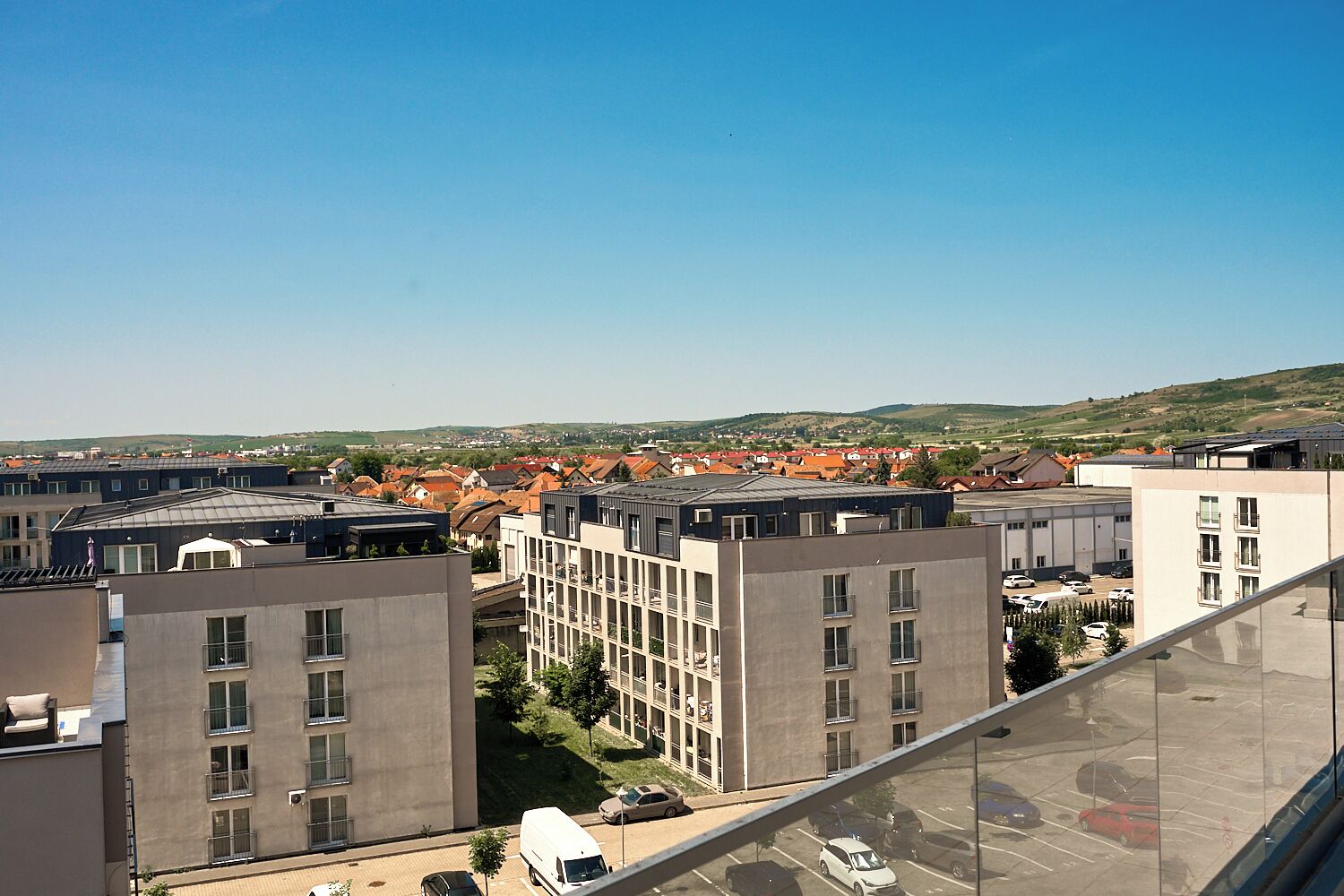 A modern building with multiple floors, a parking lot, and a view of a town with red-roofed houses.