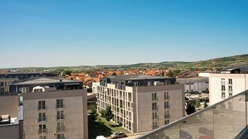 A modern building with multiple floors, a parking lot, and a view of a town with red-roofed houses.