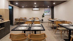 A dining area with multiple tables set for meals, wicker chairs, and a sign on the wall. - Treebo Premium Hydotel, Hi-Tech City (Hyderabad)
