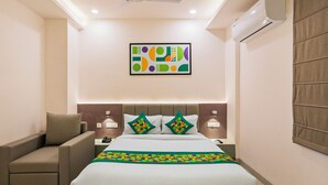 A hotel room with a bed, a chair, a nightstand, a wall-mounted air conditioner, and a ceiling fan. - Treebo Premium Hydotel, Hi-Tech City (Hyderabad)
