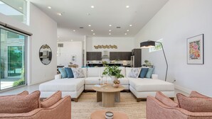 Un salon moderne avec un canapé d’angle, une table basse et un coin repas doté de meubles en bois foncé et d’un luminaire suspendu.