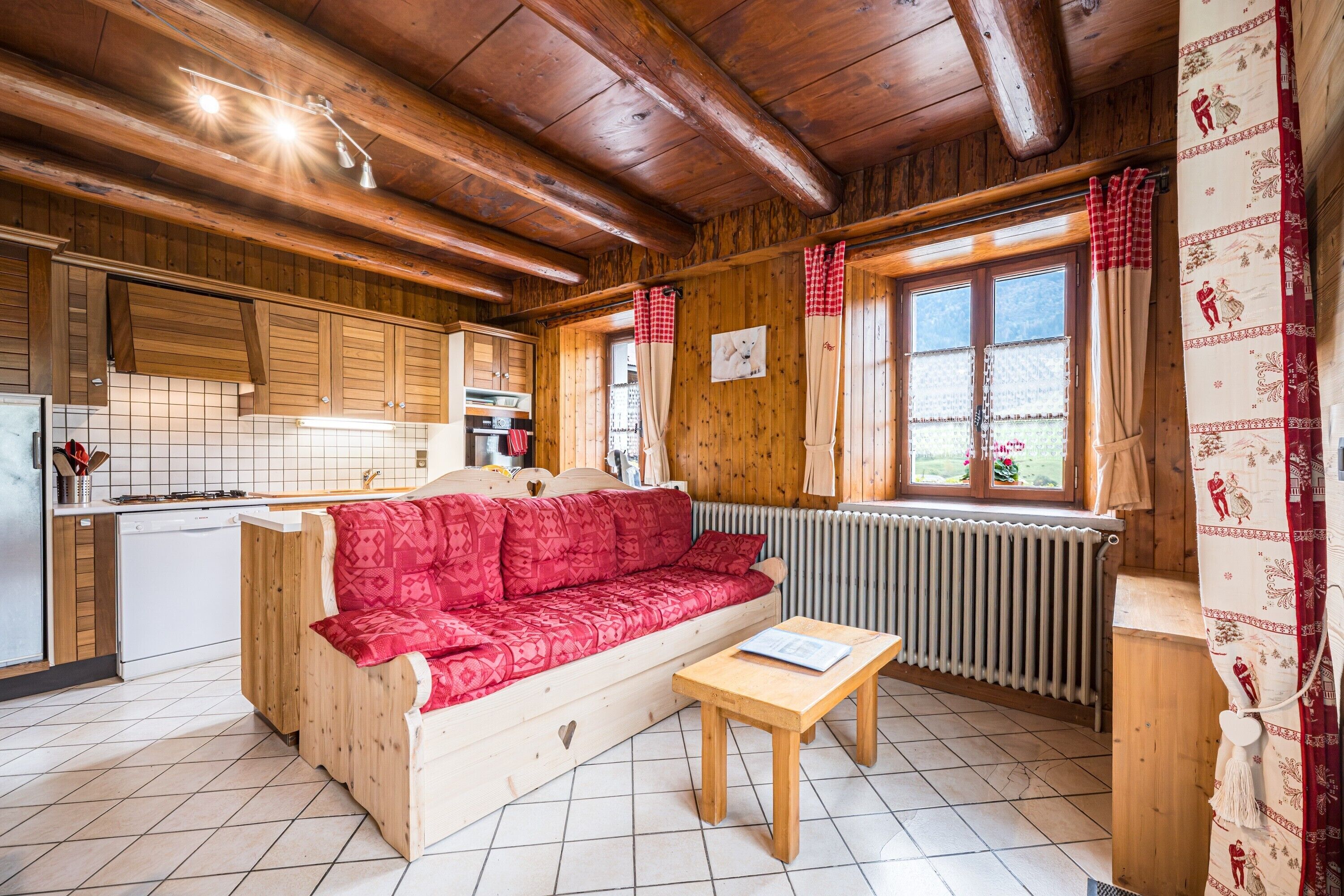 Een gezellig chaletinterieur met een houten bank, een kleine tafel, een keukenhoek en een raam met gordijnen.